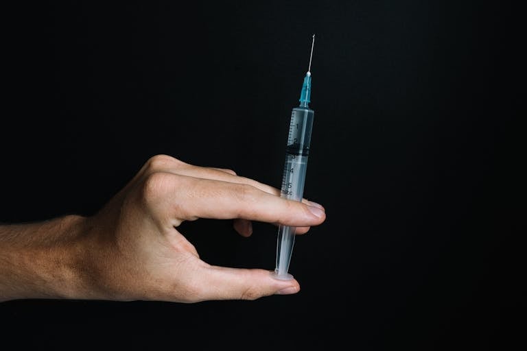 A close-up of a hand holding a syringe on a black background, symbolizing vaccination and healthcare.