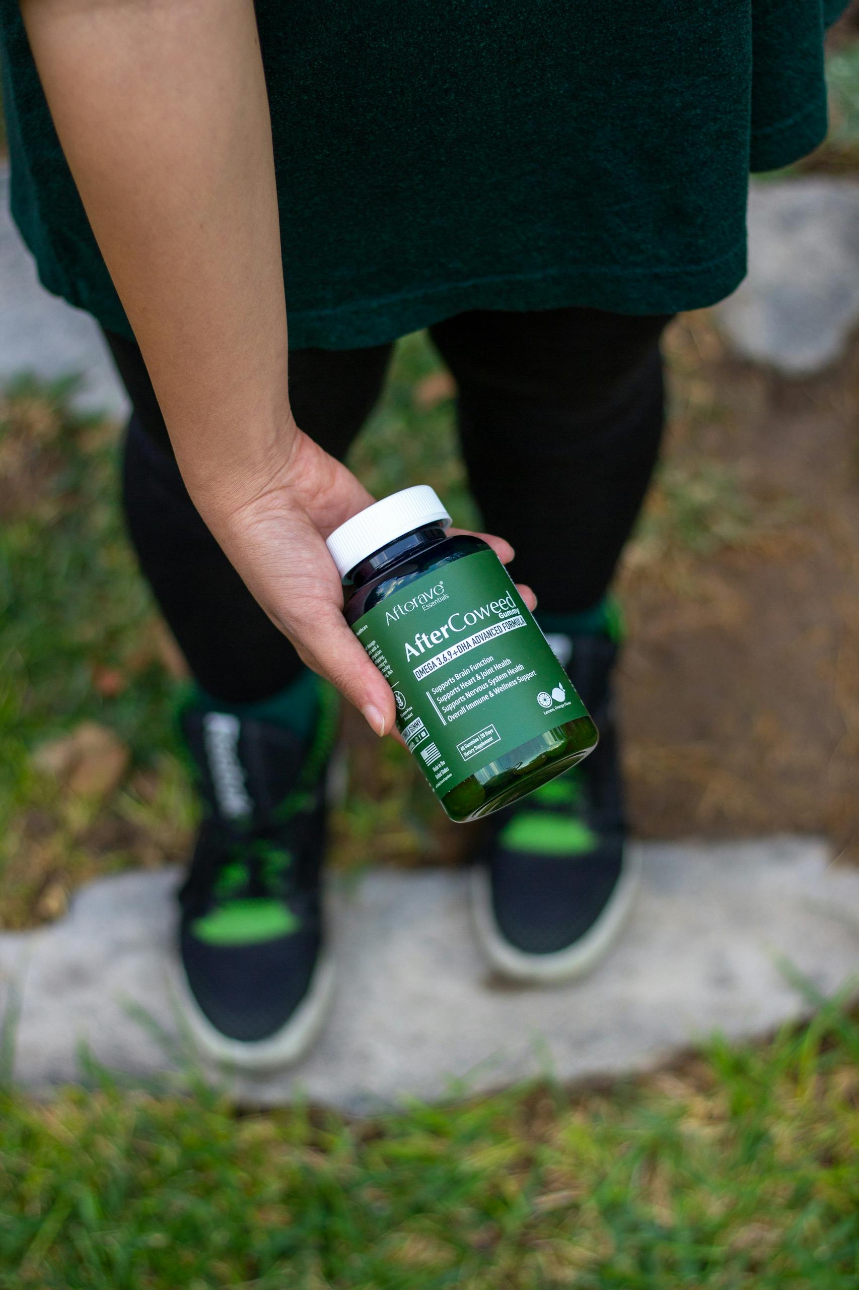 A person holds a green supplement bottle in a park setting.