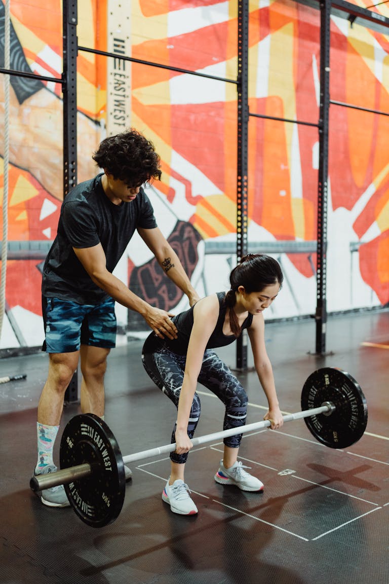 A personal trainer helps a woman with her deadlift form in a colorful gym.