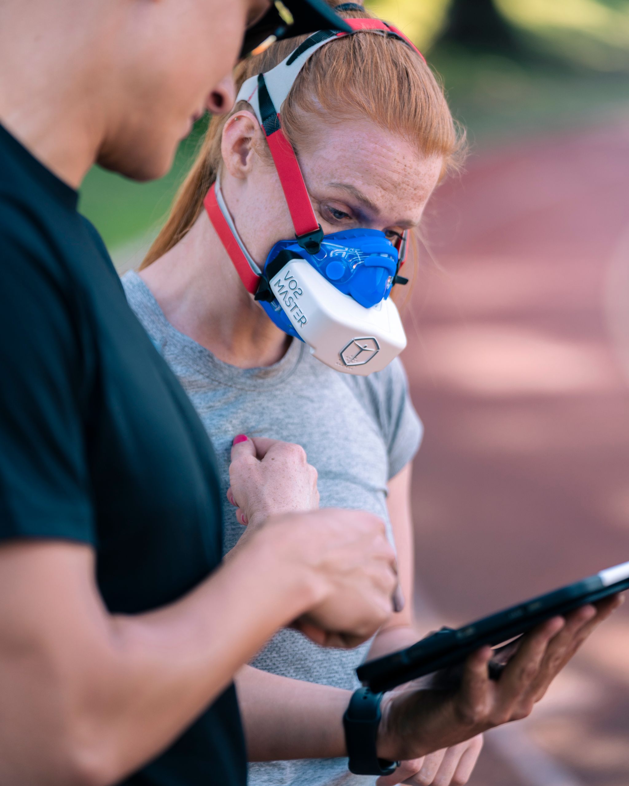 Athlete wearing VO2 master mask while consulting trainer on tablet for performance analysis.