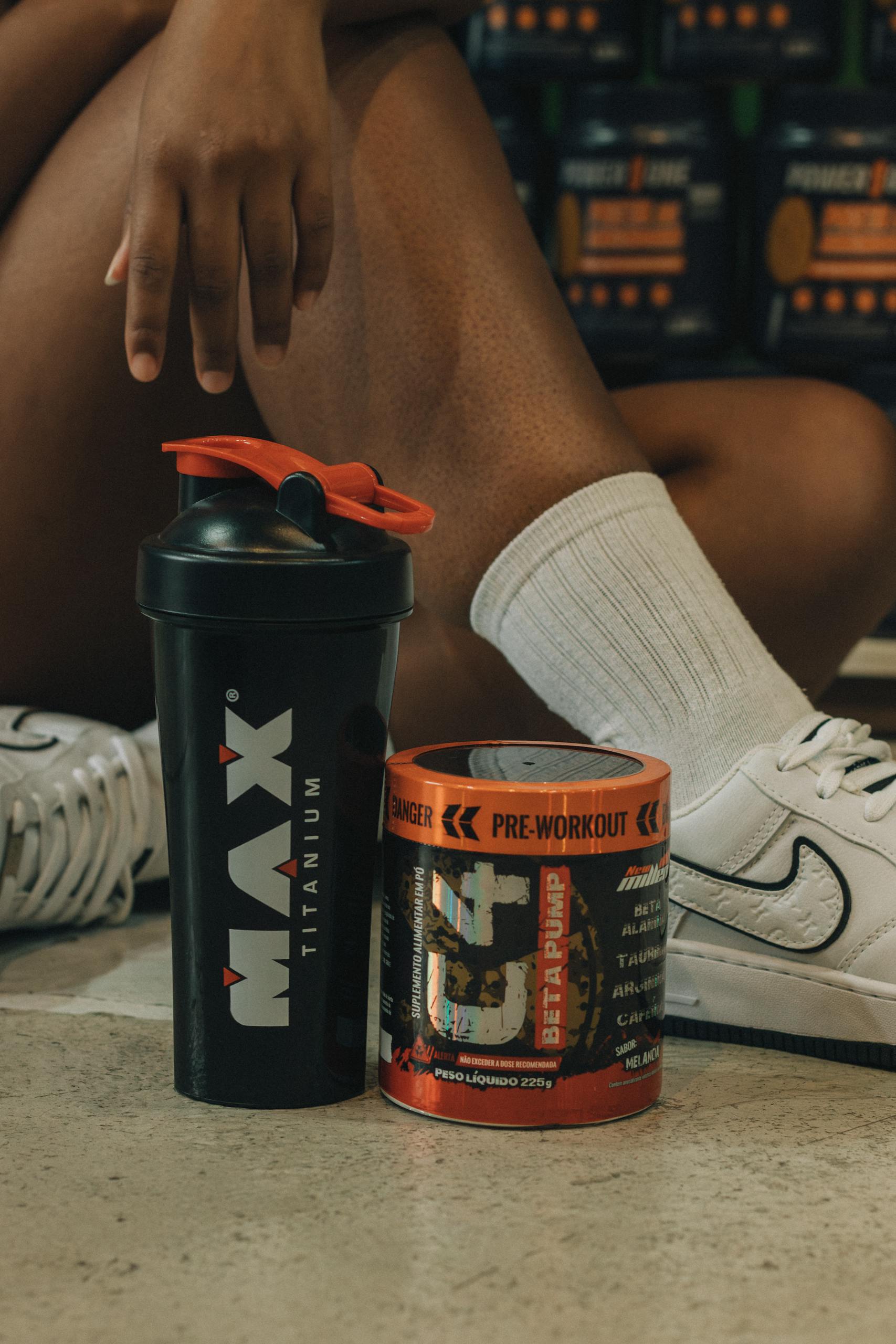 Close-up of fitness supplements and shaker with person sitting in gym attire.
