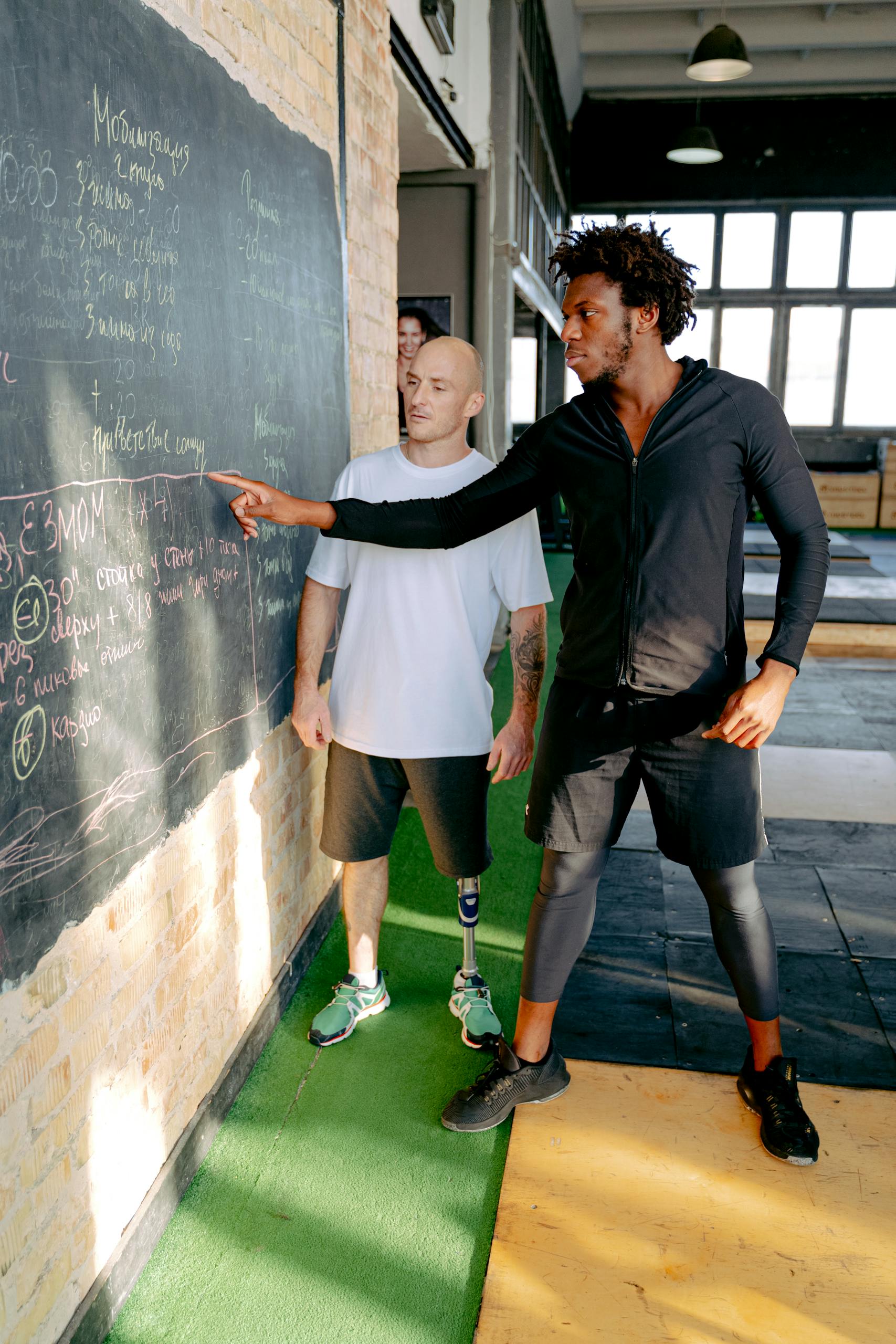Personal trainer guides man with prosthetic leg during a gym session.