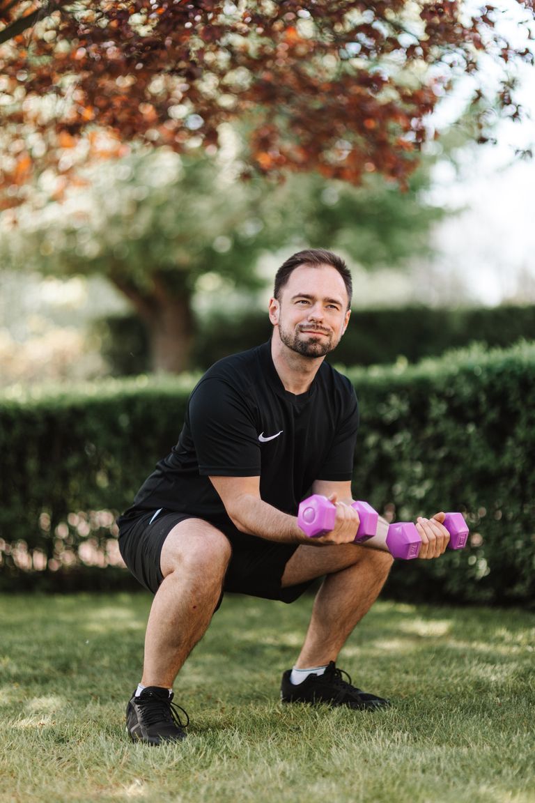 Adult male performing squats outdoors with dumbbells, capturing a healthy lifestyle in summer.