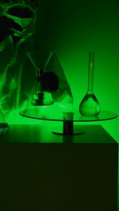 A scientist in protective gear handling glassware in a green-lit laboratory setting.